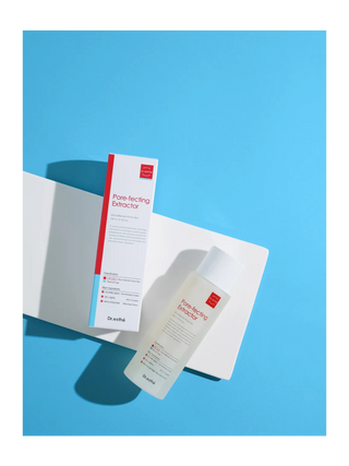 Dr. asthé Pore-faceting Extractor skincare set, featuring a white bottle and matching box with red and blue accents, styled on a white card over a solid blue background.