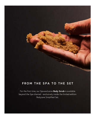 A hand holding a clump of coarse brown sugar scrub against a dark background, with promotional text below reading 'FROM THE SPA TO THE SET' and a paragraph about the body scrub.