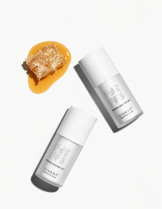 Two white Vivant Manuka Enzyme Lift Mask arranged diagonally on a white background, with a honeycomb piece and honey pool in the upper left.