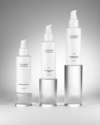 Three white skincare bottles from Vivant Cosmetics arranged in ascending size order on clear cylindrical pedestals against a light gray studio background.