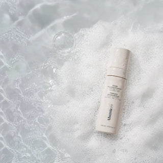 Two skincare bottles on a textured white surface with bubbles