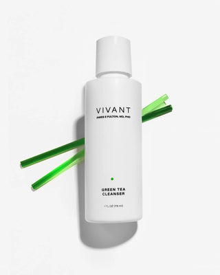A white bottle of VIVANT Green Tea Cleanser with green reed-like sticks arranged behind it on a clean white background.