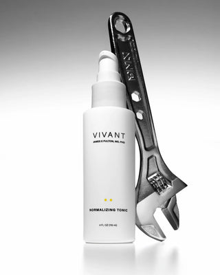 A white cylindrical pump bottle labeled VIVANT NORMALIZING TONIC stands against a dark gray gradient background, with a large metallic wrench behind it as a prop.