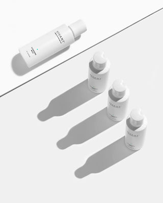 Four white skincare bottles from the brand VIVANI, arranged diagonally on a light gray surface with sharp, clean shadows.