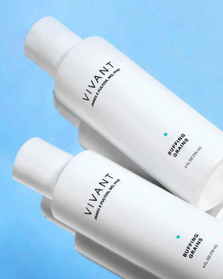Two white bottles of James Harrison Skin Pro Buffing Grains arranged diagonally on a light blue background.