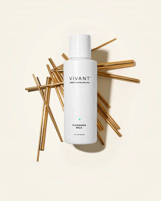 A white bottle of VIVANT Cleansing Milk centered on a warm cream background, surrounded by scattered metallic gold reed diffuser sticks. The bottle label clearly shows the brand name VIVANT.